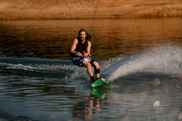 Active bearded guy holds rope and skilfully speedly riding wakeboard on the river.
