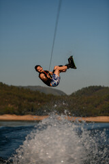 Great view of energy male wakeboarder jumping and flips on wakeboard