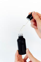 Woman's hands holding a pipette with natural oil on glass bottle