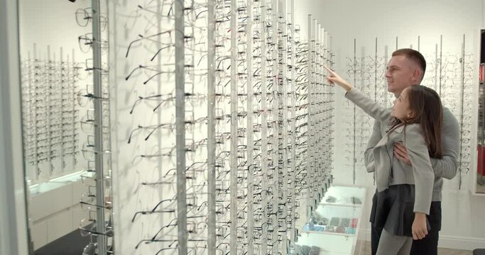 Teenage girl with father near shop window in modern optician's shop