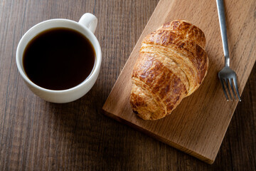 Croissant with a cup of full coffee, directly above	