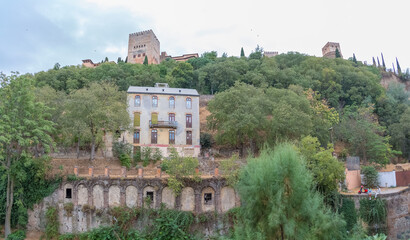 Fototapeta na wymiar View at the Alhambra citadel on top, from Paseo de los Tristes, walk of the sad (The Promenade of the Sad), classic buildings and woods around, Granada, Spain