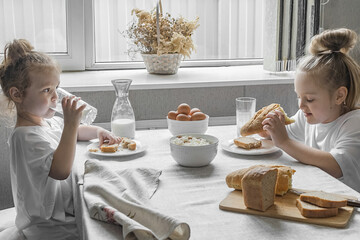 two sister girls in white t-shirts have breakfast at home in the kitchen with natural and healthy...
