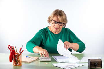 A retired woman with a calculator sorts out bills for water and electricity. The concept of accounting for household expenses, rising cost of living, rising energy prices, retirement savings