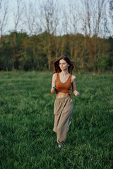Fototapeta premium A woman of athletic build runs through the park on the green grass with loose, flying hair and working out into the sunset light
