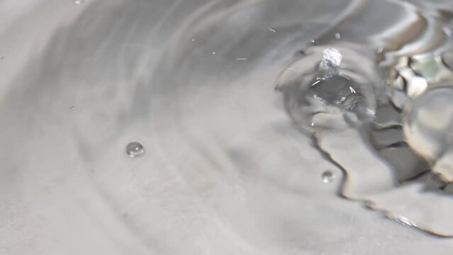 Water is dripping from a faucet into the sink. Water splashes in slow motion.