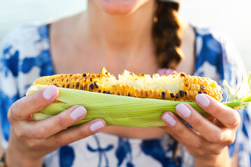 Young woman eats grilled corn on the beach. Healthy food concept. Close-up.