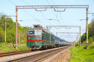 Obraz premium A powerful two-section locomotive pulls a long train of blue passenger cars to the railway station. Passenger railway transportation. Close-up view. Summer sunny weather.