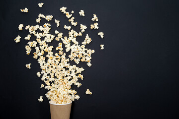 Popcorn spills out of the glass on a black background, viewed from above. A splash of popcorn