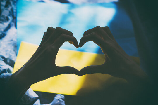 Heart shaped hands on Ukrainian flag with shadows. Vintage film photography. Ukrainian flag, creative patriotic. Stop the war in Ukraine. Stop Russian aggression. Stand with Ukraine.