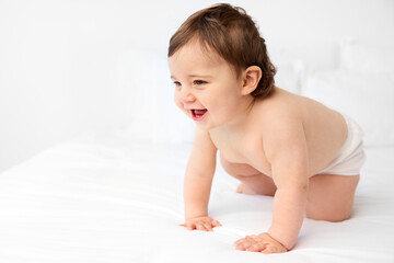 Smiling chubby baby crawling on white bed