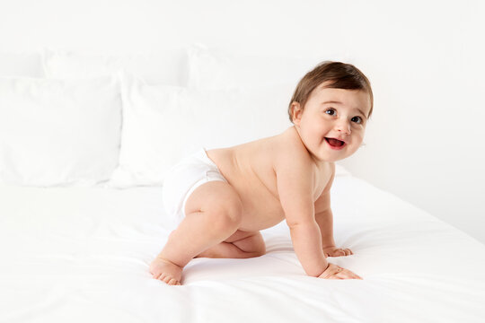 Happy chubby baby crawling on white bed