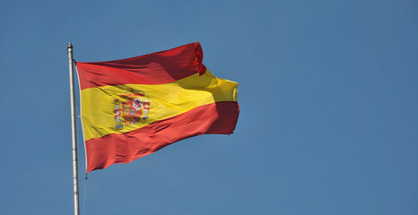 Bandeira espanhola asteada com vento a bater e com o céu por trás
