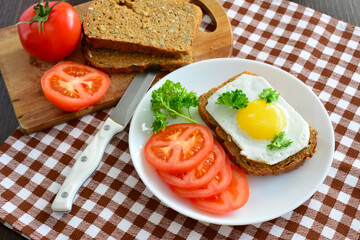 Fototapeta na wymiar healthy breakfast with wholegrain bread, fried egg and fresh vegetables on kitchen table