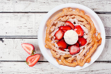 Strawberry funnel cake overhead view on a white wood background. Traditional summer fair treat.