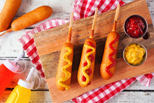 Corn dogs with mustard and ketchup. Top view table scene over a white wood background.