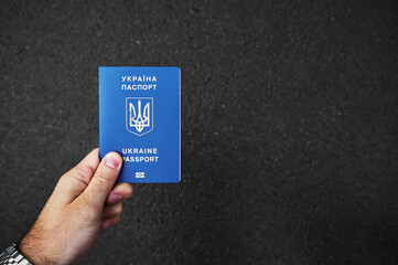A man's hand holds a battered passport of Ukraine against the background of black asphalt. Space...