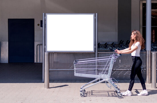 Young woman walks past to a white billboard with an empty shopping cart