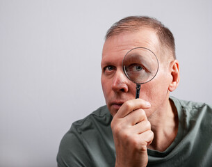 Mature man looking at magnifying glass and checking or investigating smth, studying thoroughly information. Spy, accountant, auditor job. High quality photo