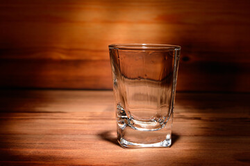 An empty glass on a wooden table. with the remains of an alcoholic beverage on the walls of the...
