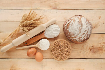 Products for baking bread. Wheat, grain, flour in a spoon, rolling pin, round bread, eggs on a light wooden board. Agro-industry and culinary.