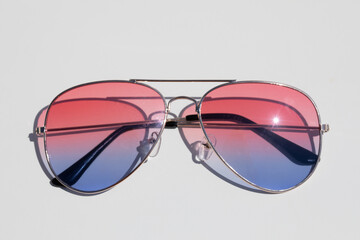 The sunglasses with pink and blue lenses lie flat on a white surface. Illuminated by strong sunlight. Vacation and well-being concept. - 504634102