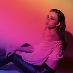 Sexy young girl in the purple red light of the party, she is in leather pants and a top, 90s style