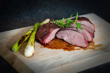 ready to eat, grilled chamois meat with spring onions and rosemary on a wood board