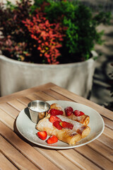 pancakes decorated with strawberries on a white plate standing on a wooden table, breakfast