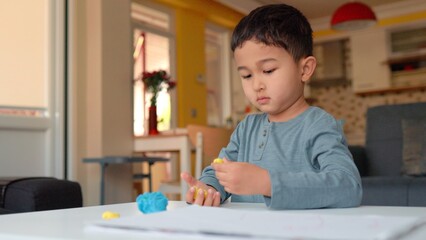 Little asian preschooler engaged in creativity. Boy takes a colourful clay and sculpts figures