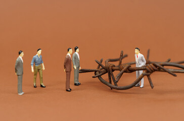 On the brown surface of the figurines of businessmen, one businessman is isolated from the others with barbed wire.