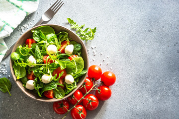 Green salad with fresh leaves, tomatoes and mozzarella at stone table. Top view, copy space.