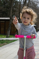 Child on a scooter in the park. A little girl rides a scooter on a sunny day. Active sports for preschoolers
