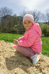 Little girl in the sandbox with shovels and a bucket on the playground. Child outdoors in summer. Summer fun. Summer sunny day in the sandbox.