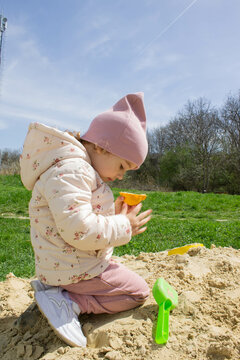 Little girl in the sandbox with shovels and a bucket on the playground. Child outdoors in summer. Summer fun. Summer sunny day in the sandbox.