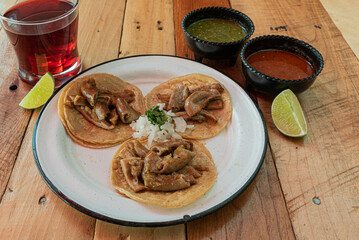 Tradicionales tacos mexicanos de tripa servidos en una mesa con salsas y agua fresca de jamaica 