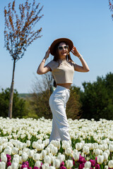Obraz premium A beautiful slender woman in a hat stands in a blooming field of tulips. Spring time