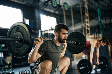 Male athlete doing barbel back squat exercise while working out at gym.