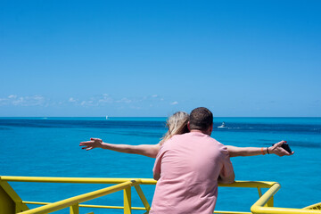Rearview of a couple with arms outstretched in a ship against the blue sky, Isla Mujeres Mexico