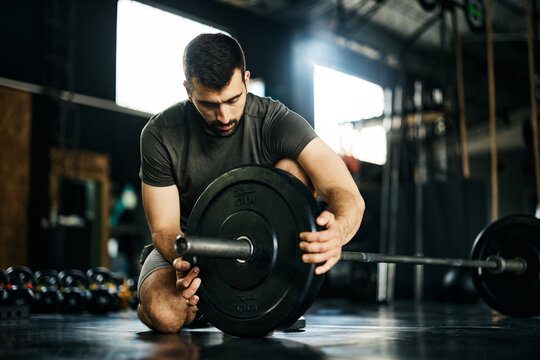 Male Athlete Adding Weight Plate On Barbel Before Sports Training At Gym.