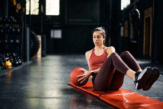 Female athlete doing sit-ups with medicine ball while working out in health club.