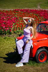 A girl model in casual clothes sits on a red car among tulip fields.