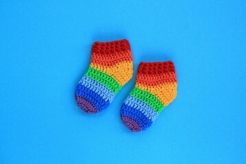 Rainbow handmade crochet baby socks booties on blue background. Baby shower greeting card, poster, banner top view concept