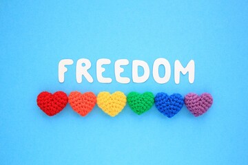 Crochet hearts rainbow colors and Freedom lettering on blue background. LGBT flag gay pride community, equal rights movement and gender equaluty life concept. Flatlay idea for postcard, banner, poster