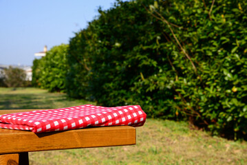 Folded red and white checkered tablecloth on wooden picnic table in park