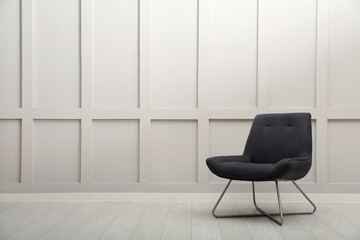 Modern grey armchair near white wall indoors. Space for text