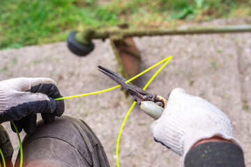 A gardener with a pruner cuts a piece of fishing line for a gas mower. Spring lawn mowing, lawn care