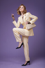 High fashion photo of a beautiful elegant young woman in a pretty beige cream linen suit, jacket, trousers, pants, blazer, handbad on purple lilac background. Hairstyle, slim figure. Studio Shot