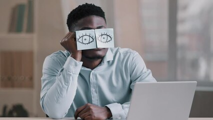 Sleepy funny african american office manager business man sitting at home workplace with sticky notes on eyes comic young tired worker has sleeping problem napping at desk wears glasses with stickers