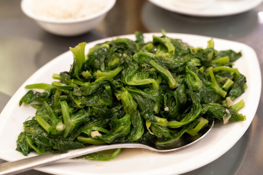 Simple and healthy stir fried oriental green vegetables with garlic served in white plate at restaurant